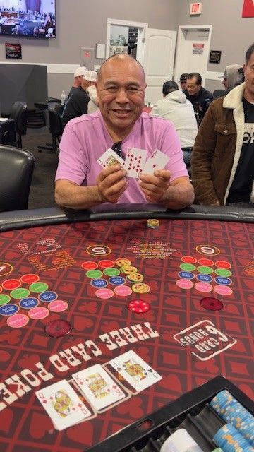 Man smiling at a casino table, holding playing cards with poker chips and cards spread out nearby.