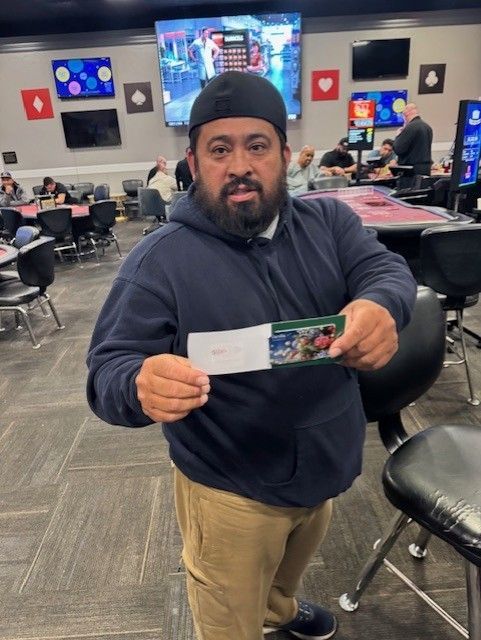 Man holding a ticket or card in a casual lounge with TVs and red-and-black tables behind him