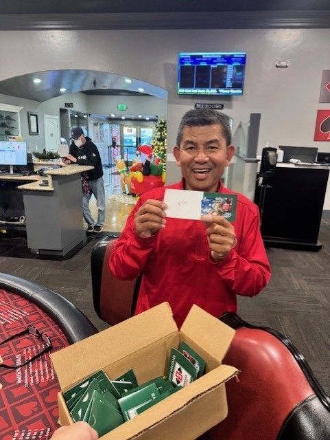 Smiling person in a red jacket holding a card in a bowling alley, with a box of green packages nearby