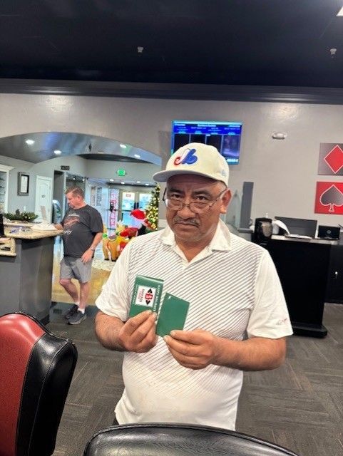 Man holding two green cards in a casino, wearing a white cap and shirt, with slot machines in the background