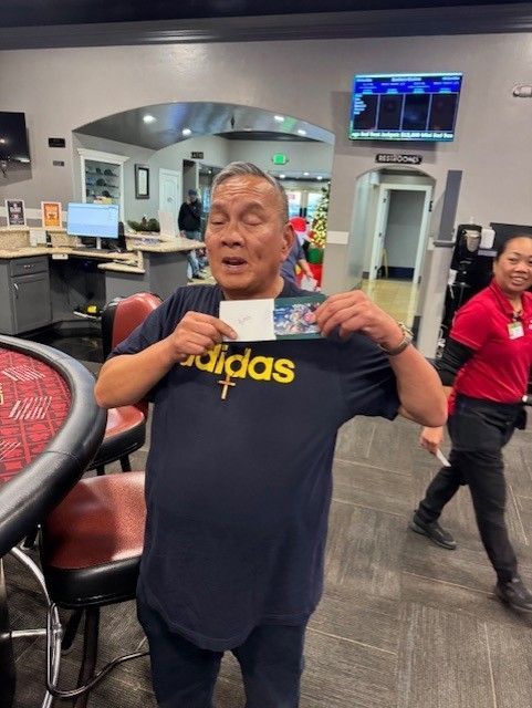 Man holding up a navy Adidas shirt in a gym lobby, smiling near exercise equipment.