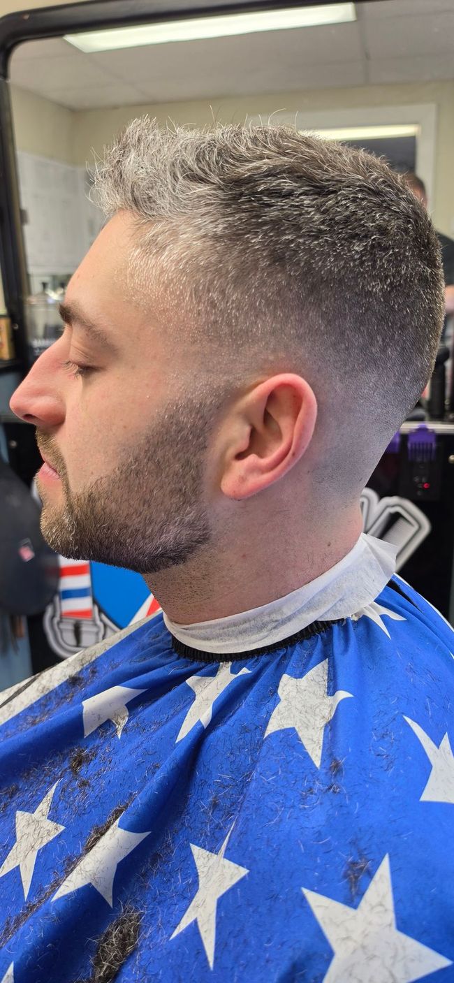 Side-profile haircut in progress at a barbershop, with a blue star-patterned cape around the client