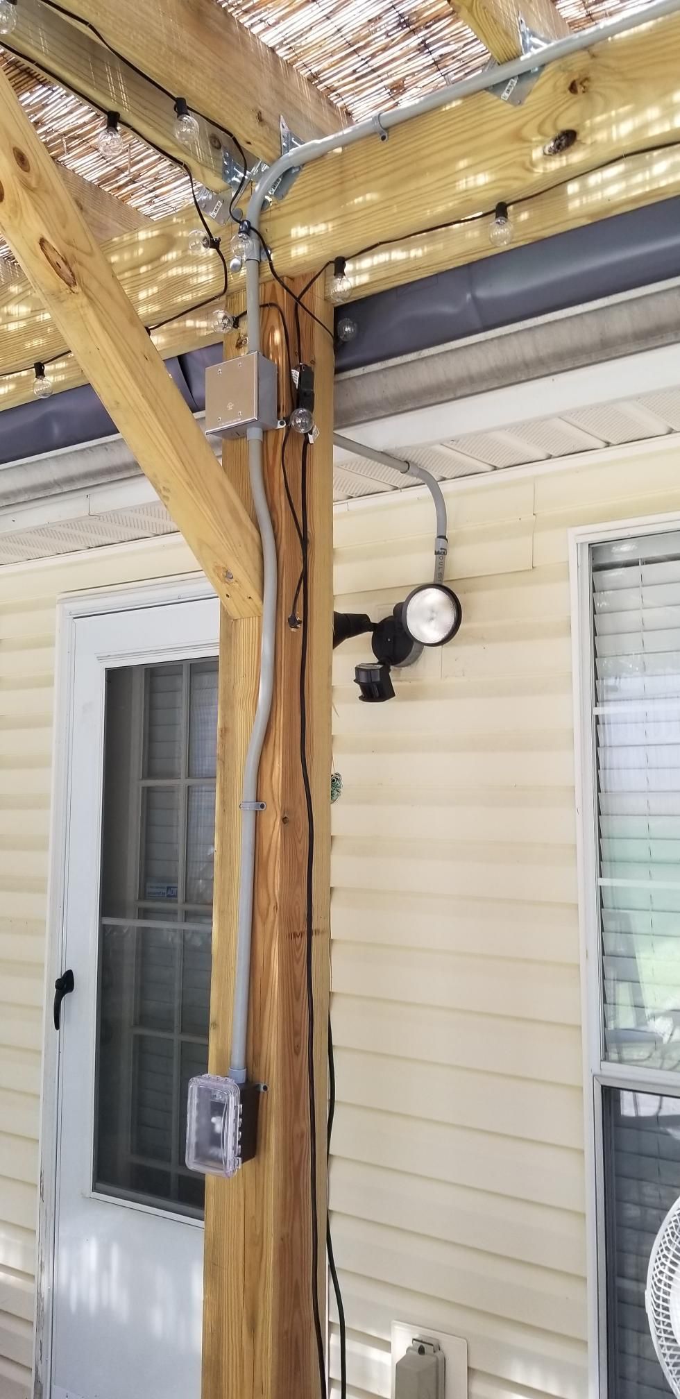 Wooden porch post with electrical outlet and light under a covered patio beside a house window