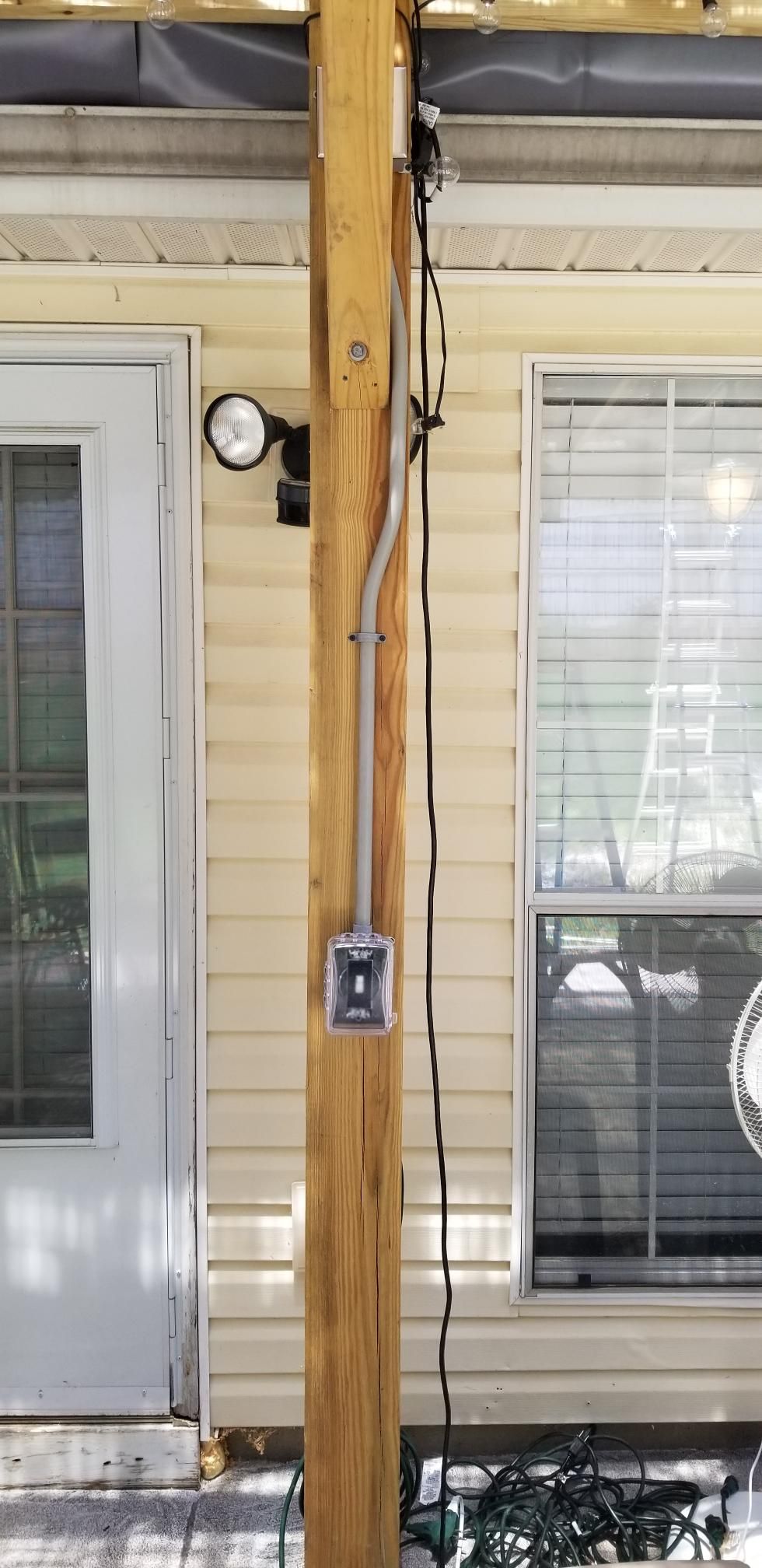 Wooden porch post with an outdoor electrical outlet and cable between two glass doors