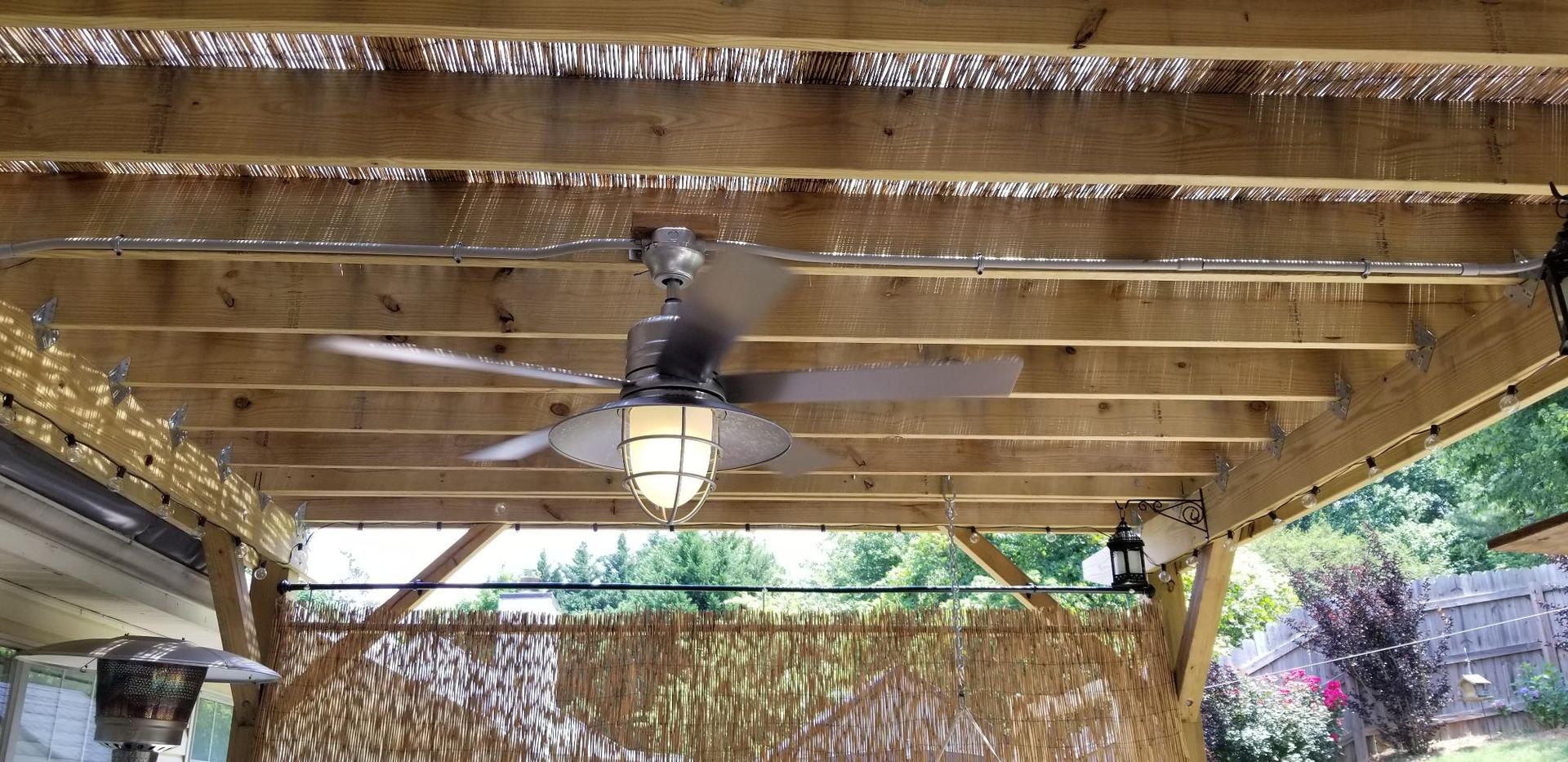 Wooden pergola ceiling with a hanging lantern and woven bamboo shade, viewed from below
