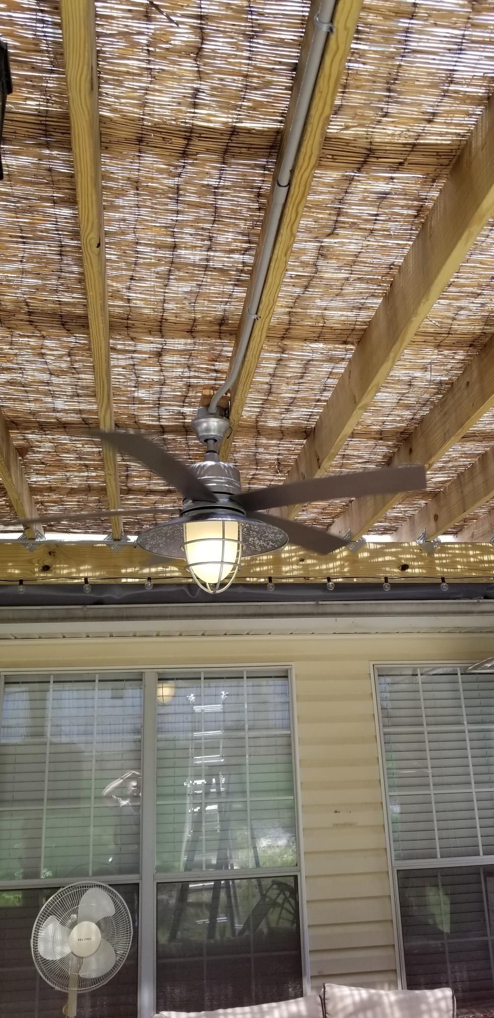 Covered patio ceiling with bamboo slats, a black ceiling fan, and windows below