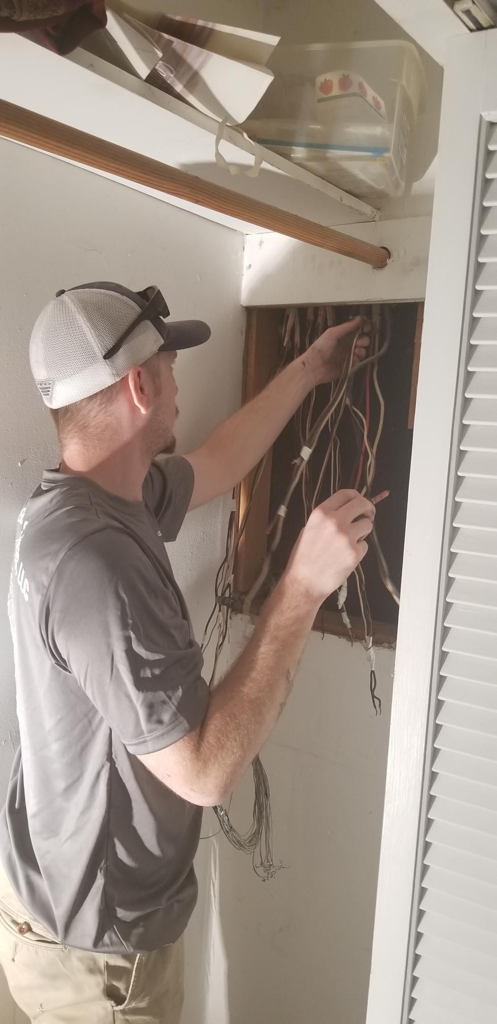 Worker wiring a wall-mounted electrical panel in a utility room, holding bundled cables.
