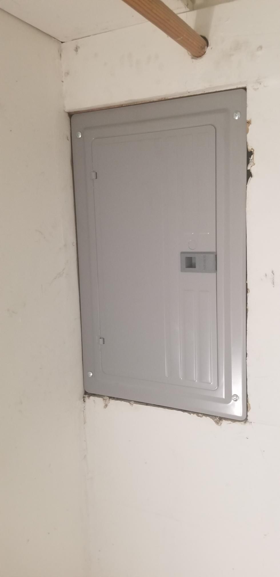 Gray electrical panel on a white interior wall, with exposed edges and a small latch.