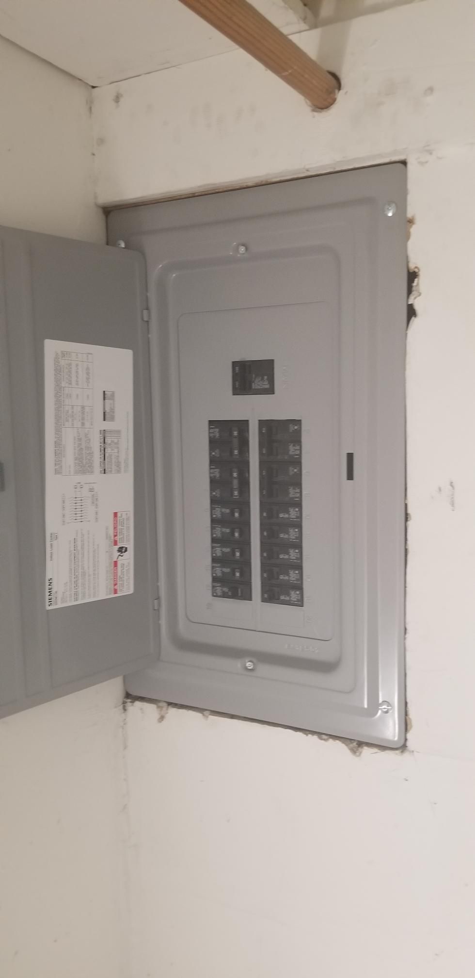 Open electrical breaker panel recessed in a white wall, door open.