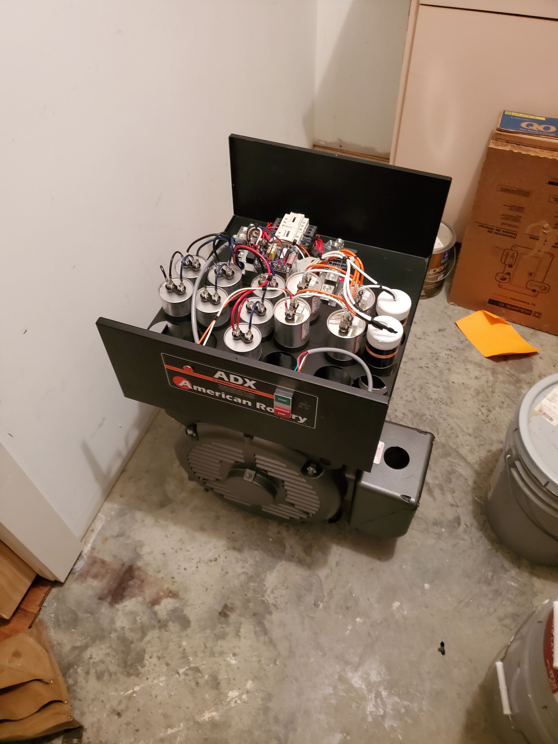 Black electronic device with open top, multiple components, fan, in a corner on concrete floor.