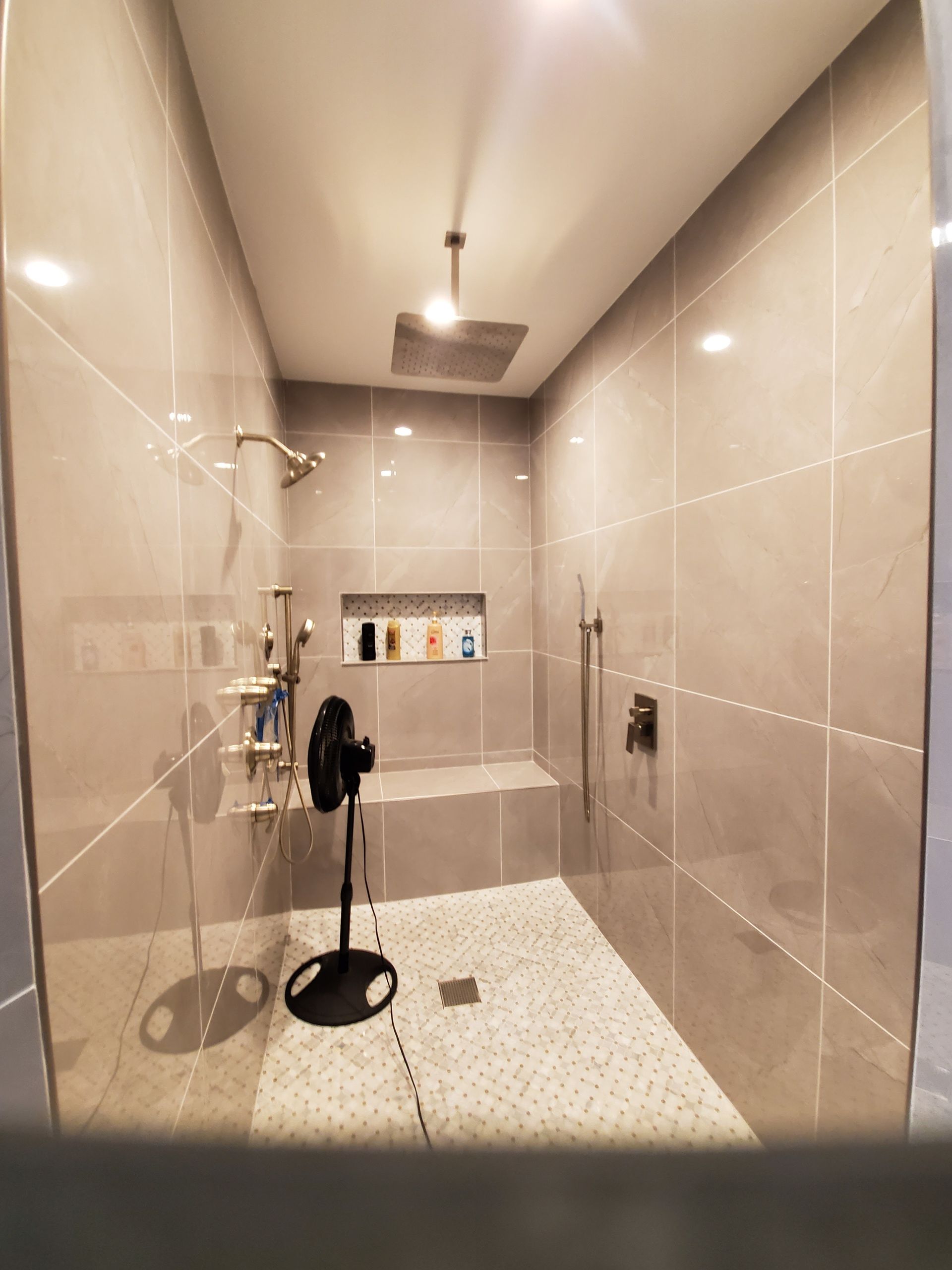 Spacious tiled shower with a built-in bench, overhead rain shower, and a small fan.