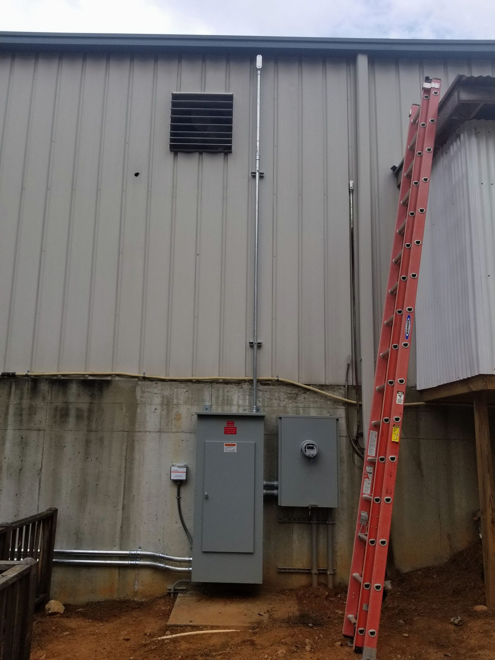 Electrical panel and conduit mounted on a gray building, with an adjacent ladder.