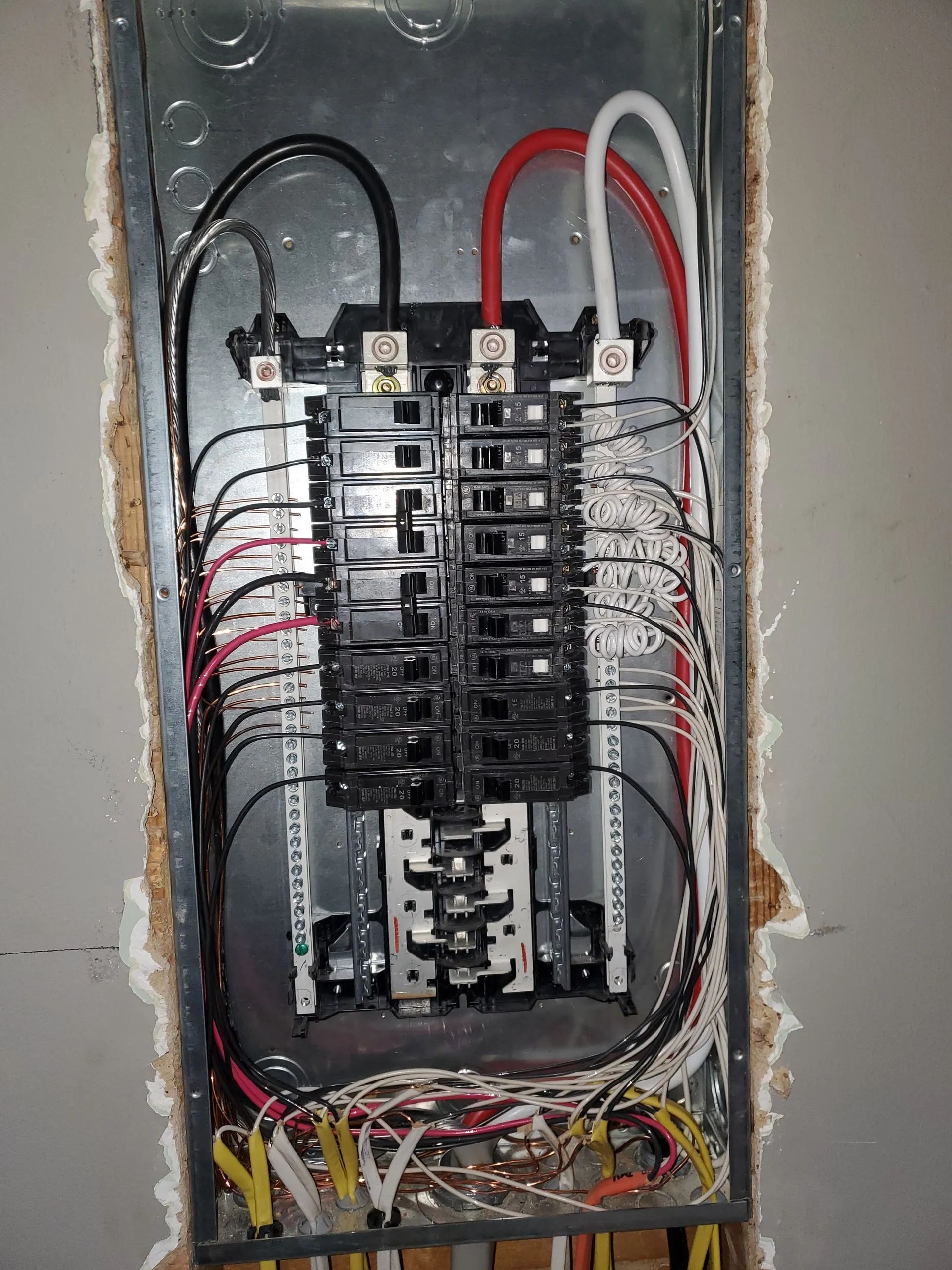 Open electrical breaker panel with exposed wiring and black, red, and white cables