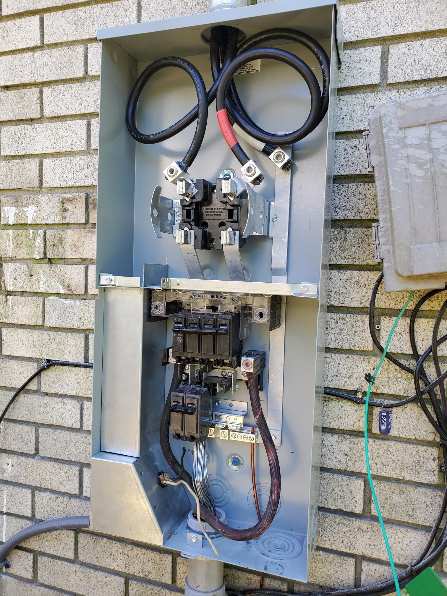 Open electrical breaker panel on a brick wall with exposed wires and components