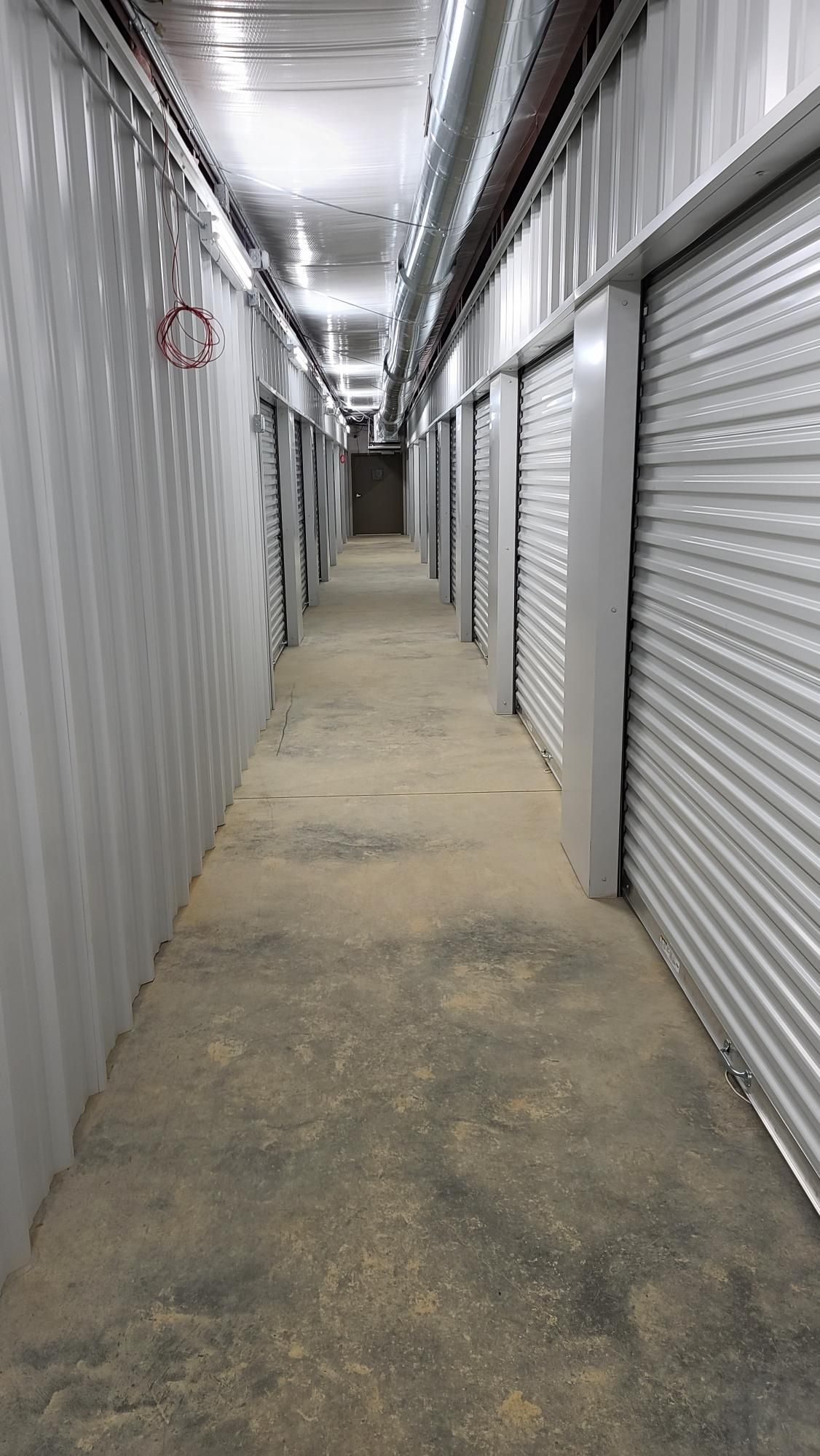 Narrow storage hallway with metal roll-up doors on both sides and a concrete floor.