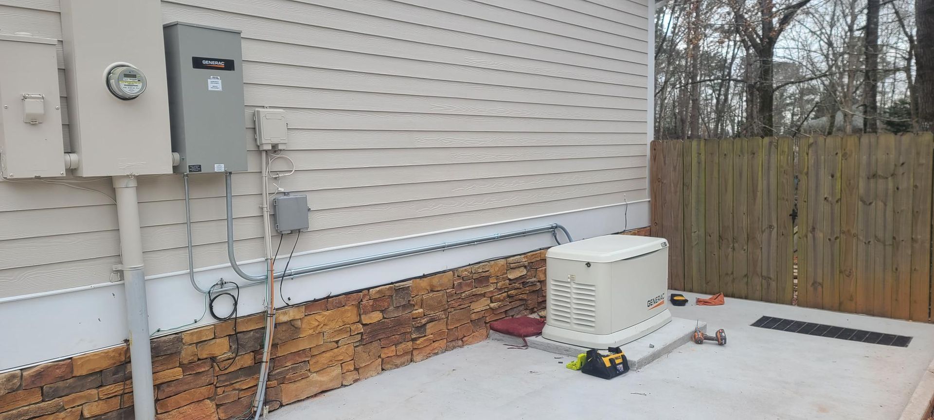 Backyard patio beside a house with utility meters, HVAC unit, and a wooden fence in the background