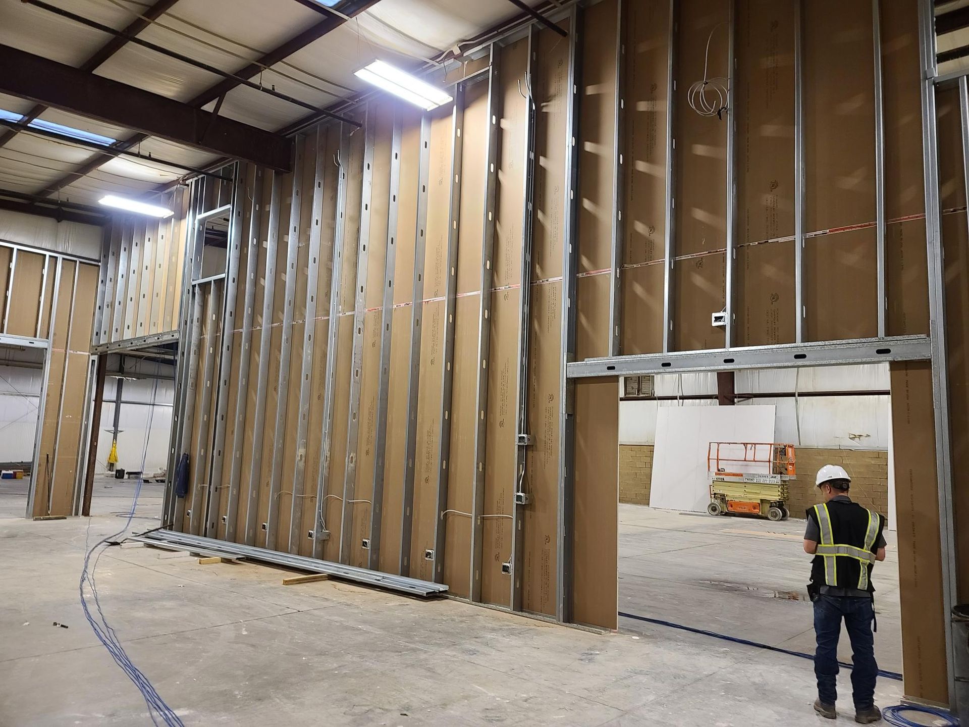 Large warehouse interior with exposed wall framing and a worker in a hard hat near an opening.