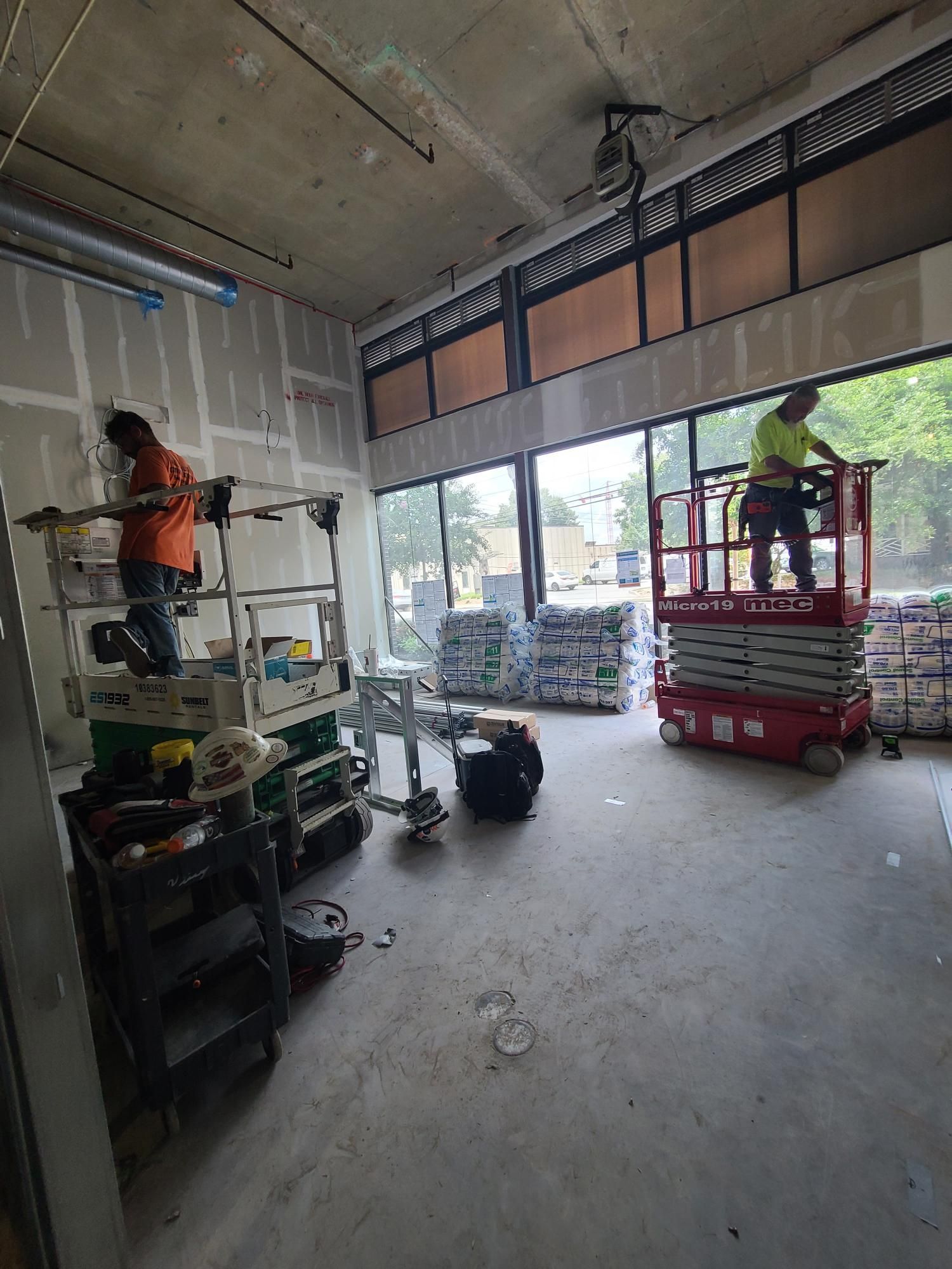 Workers using scissor lifts inside an unfinished building with exposed walls and open garage doors