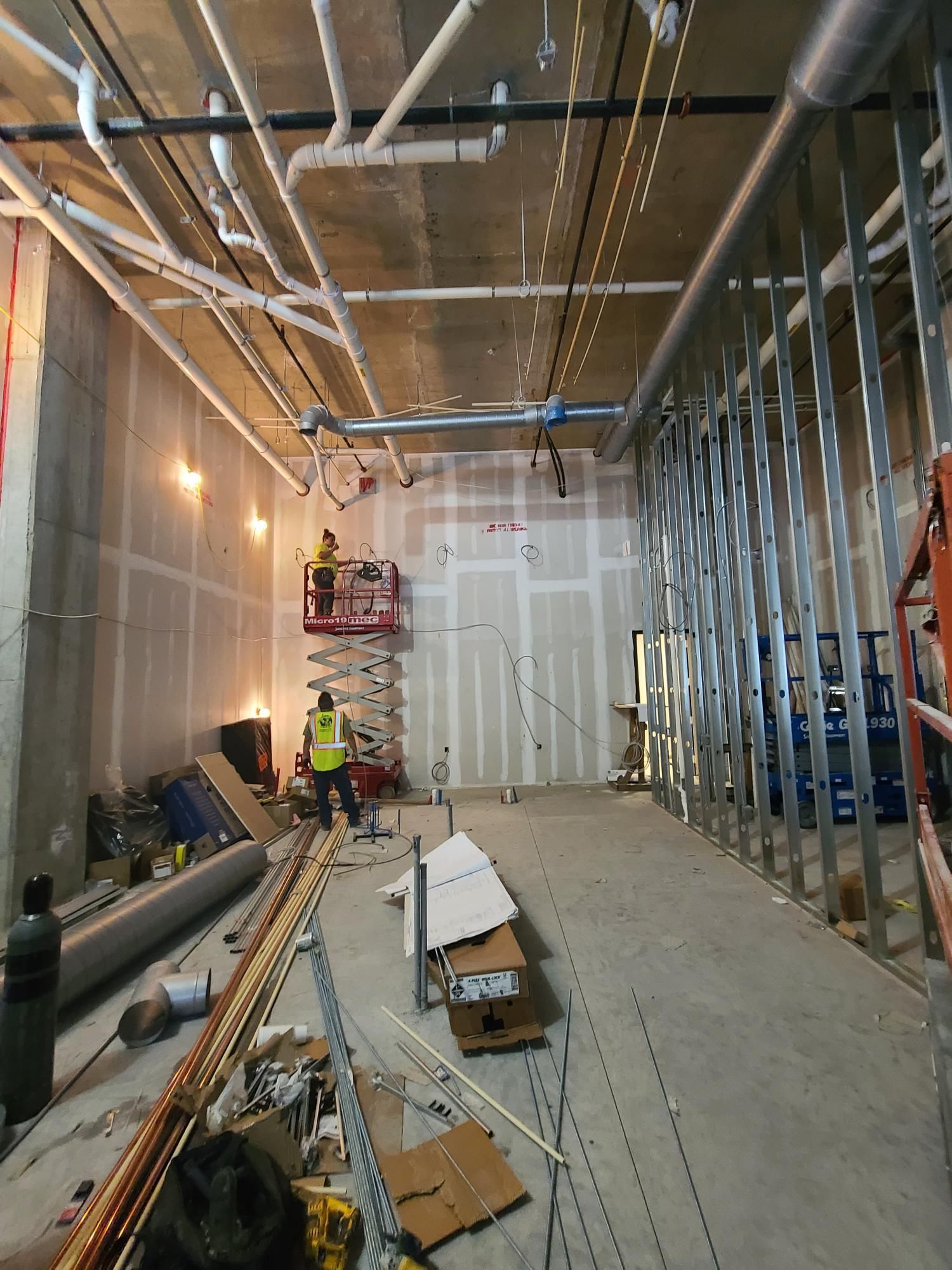 Interior construction site with exposed wiring, metal studs, drywall, and materials stacked along the floor.