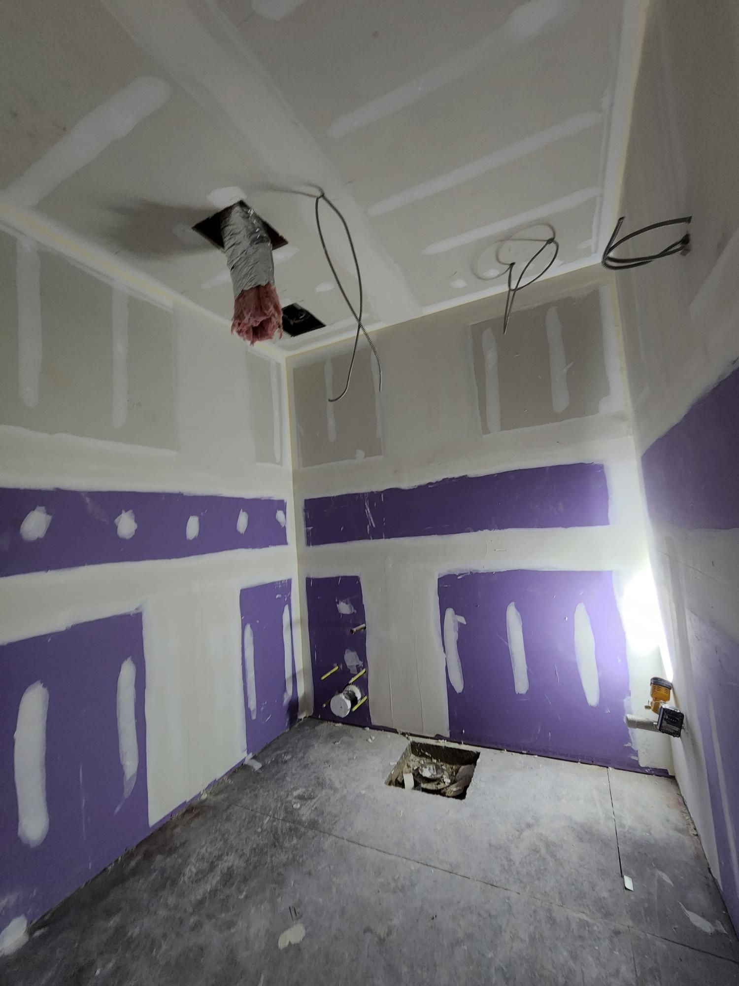 Unfinished room with purple drywall patches, exposed ceiling wiring, and bare concrete floor.