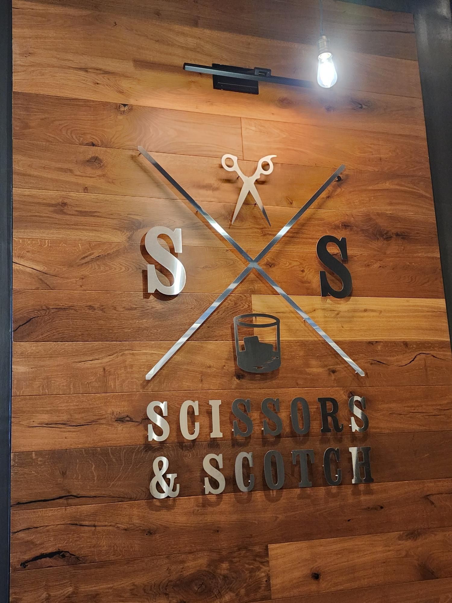 Wood sign with crossed scissors and the words “Scissors & Scotch” on a wooden wall