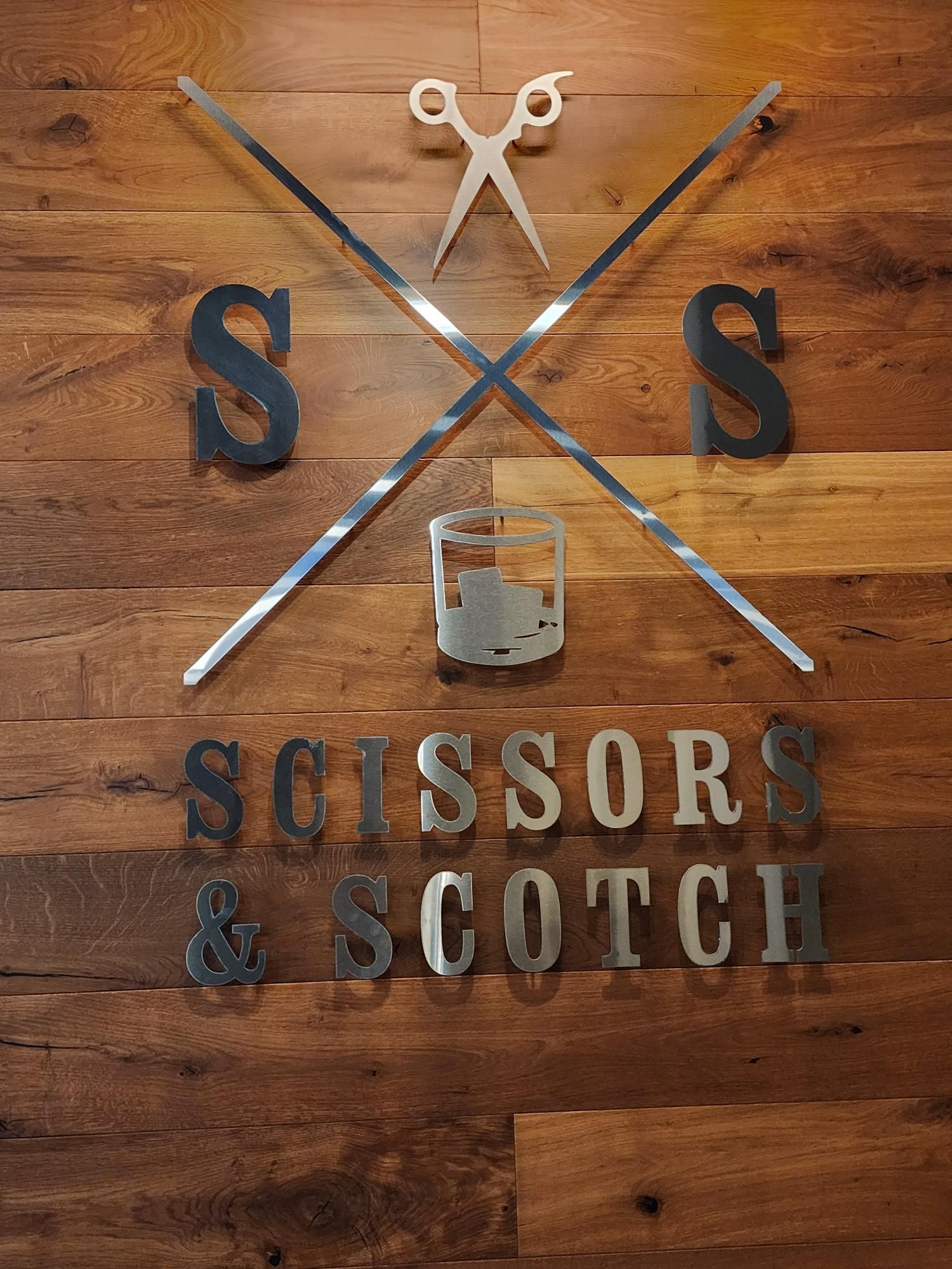 Bar logo on wood wall reading “Scissor & Scotch,” with crossed scissors and barber poles.
