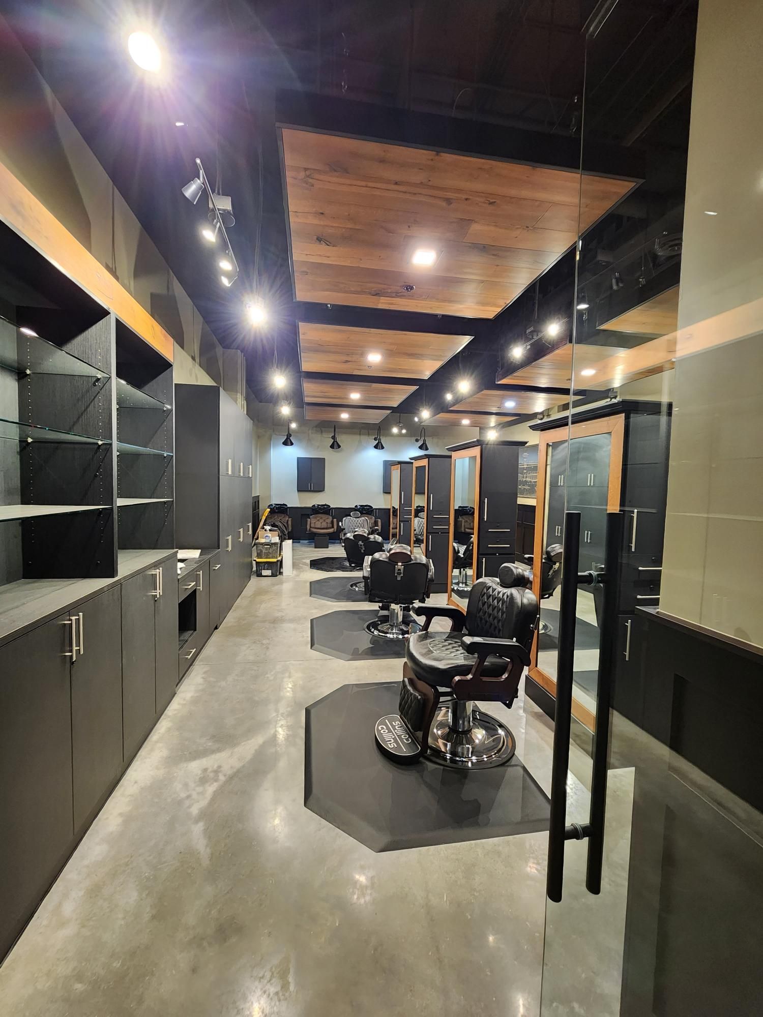 Modern hair salon interior with styling chairs, mirrors, black cabinetry, and wood-accent ceiling lights.