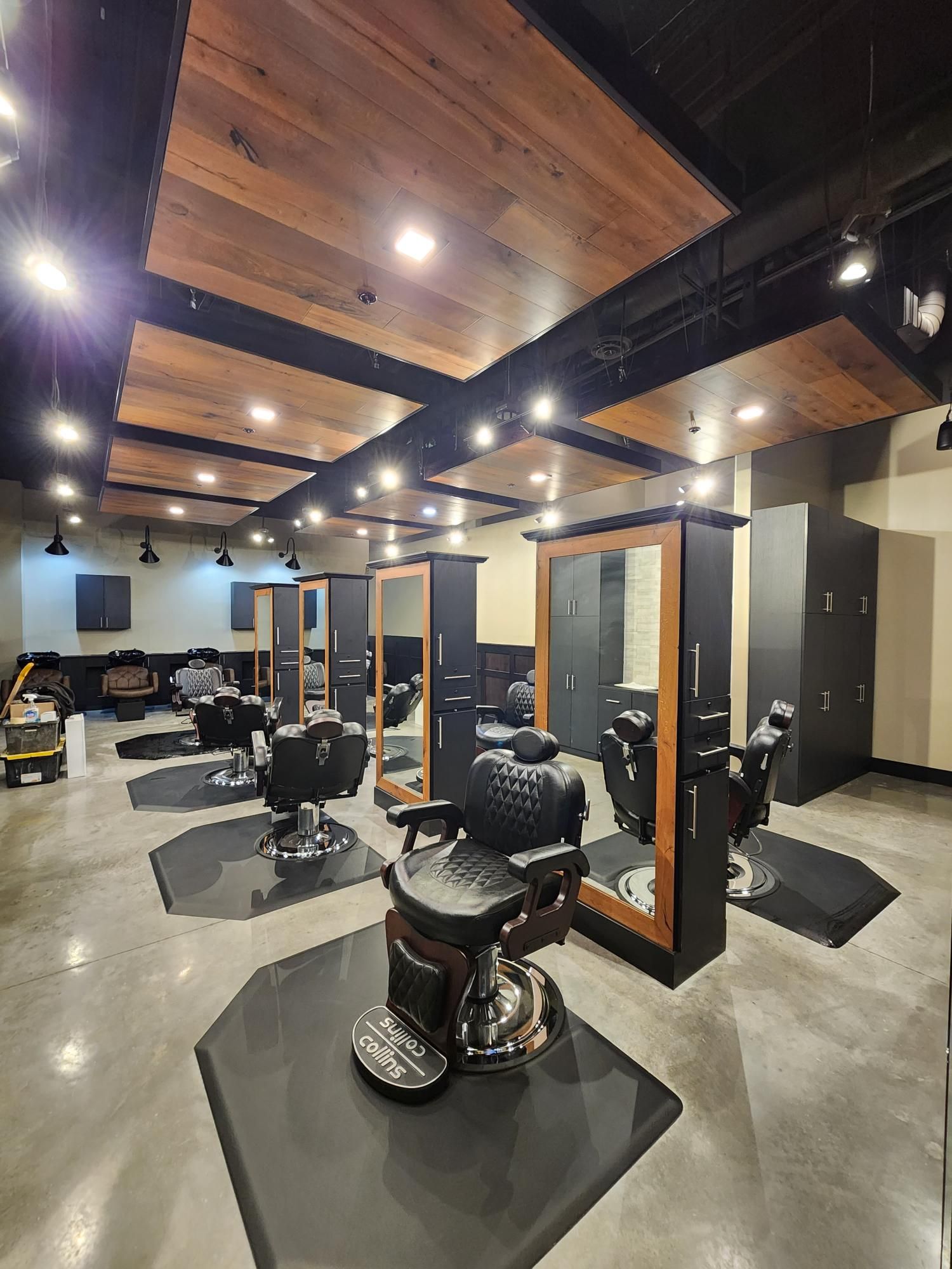 Empty barber shop with multiple chairs, mirrors, and black-and-wood ceiling panels.