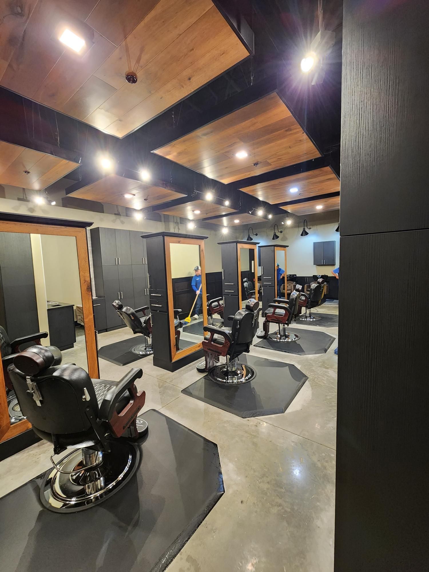 Modern barber shop interior with black chairs, mirrors, and wood-paneled ceiling under bright lights