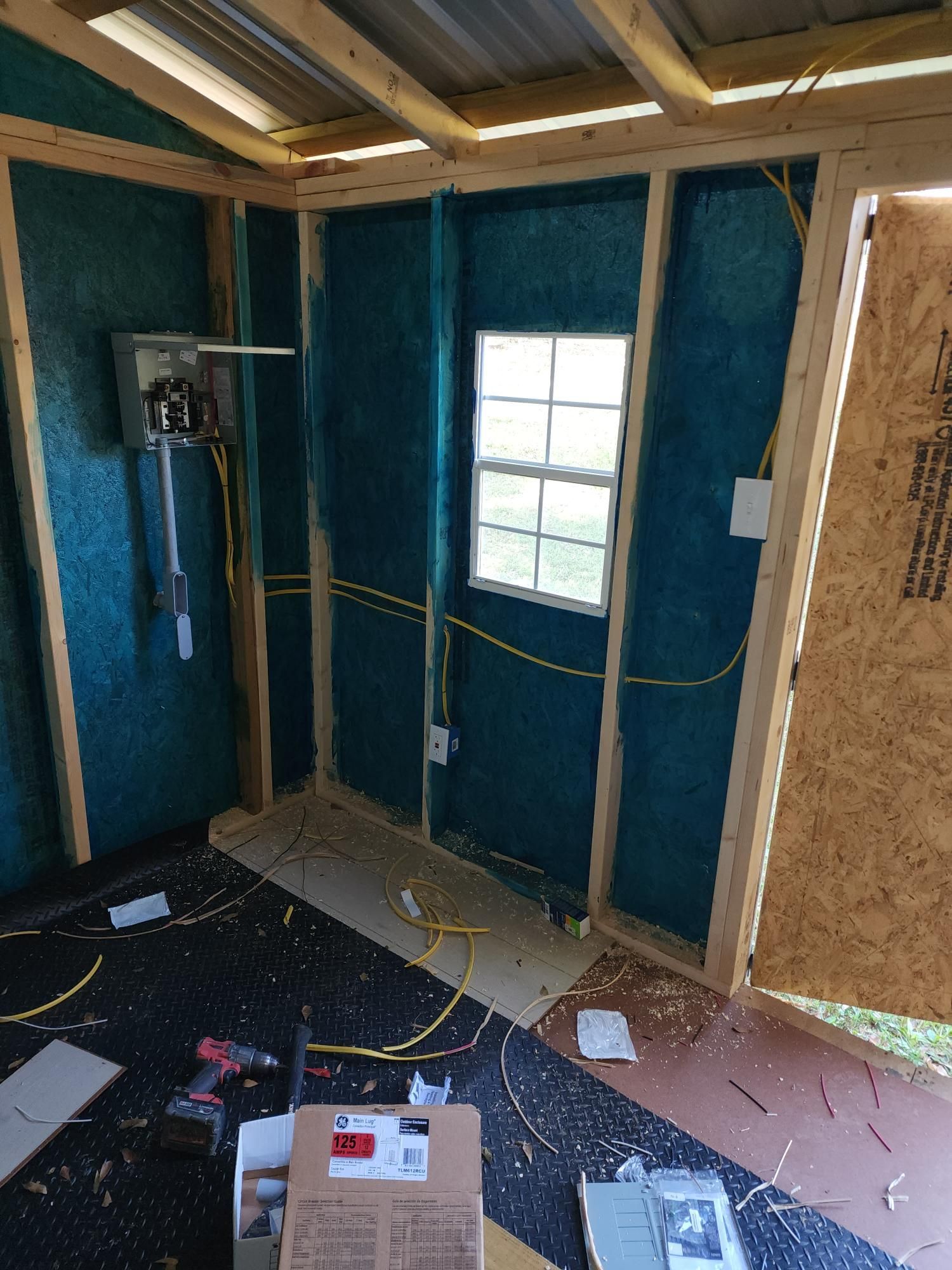 Unfinished room with blue insulation walls, exposed studs, a window, and construction debris on the floor