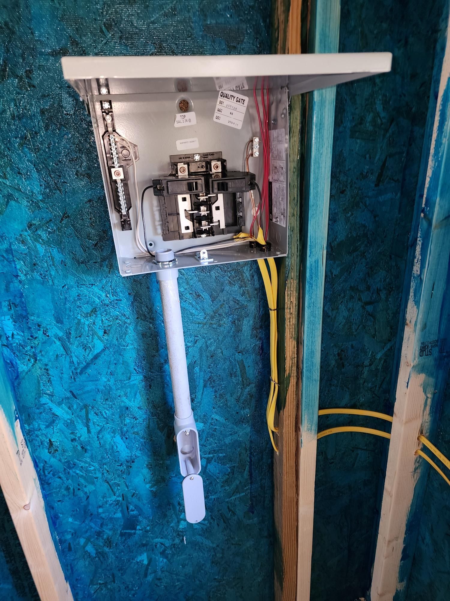 Electrical breaker panel mounted on a blue wall, with exposed wiring and open cover.
