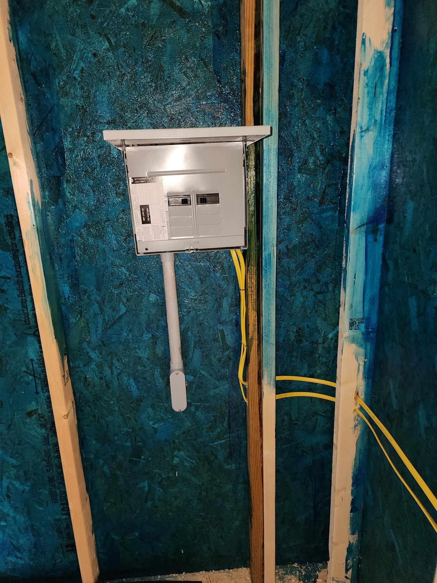 Electrical meter box mounted on blue insulation between exposed wall studs with a yellow cable nearby