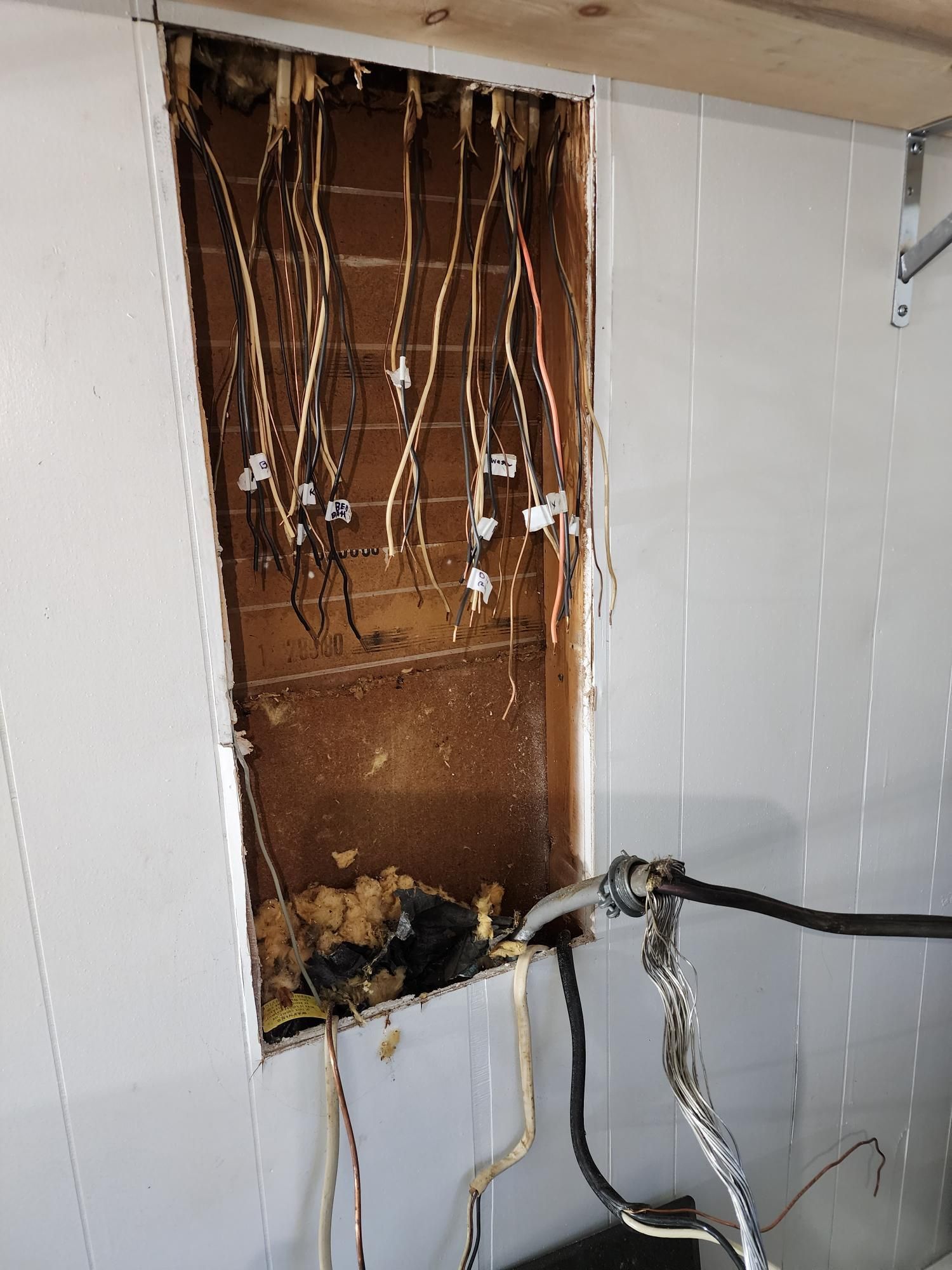 Open wall with exposed electrical wires and damaged wiring, showing a hazardous unfinished repair area.