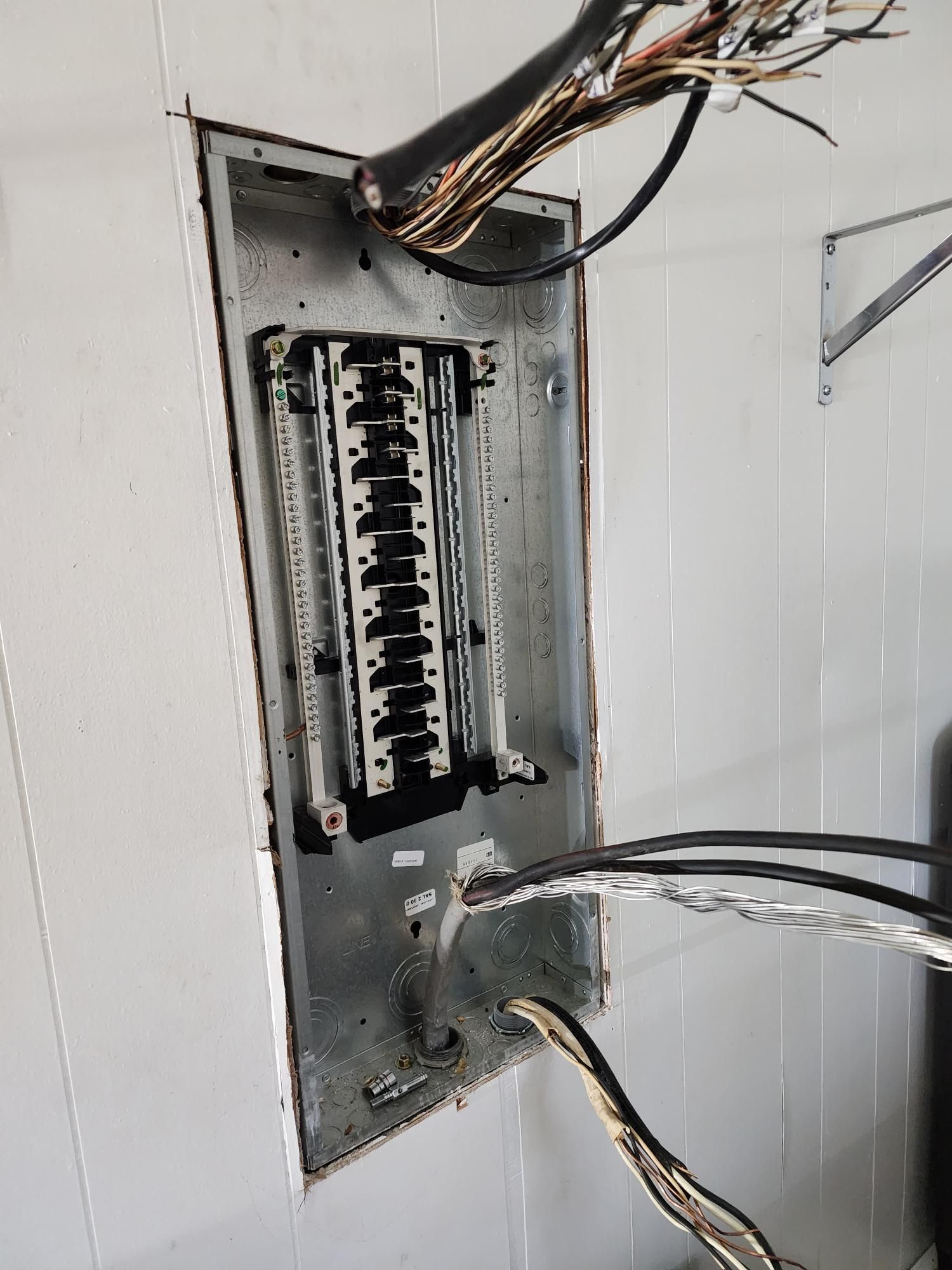 Open electrical breaker panel with exposed wires in a wall opening