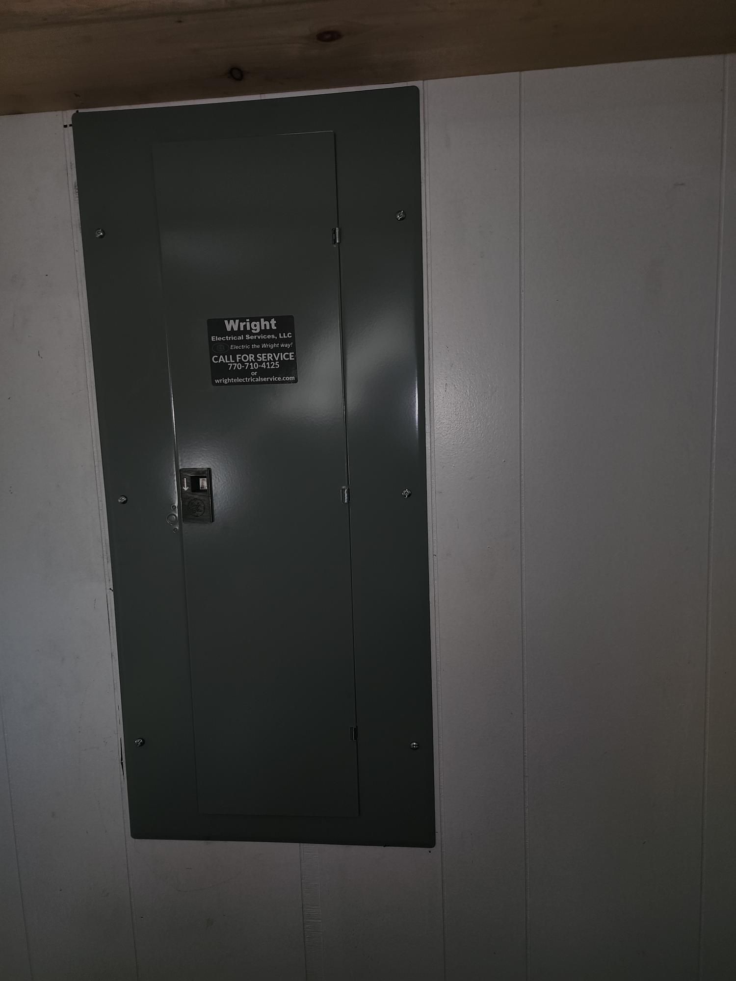 Green electrical panel on a beige wall with a small warning sign and handle.