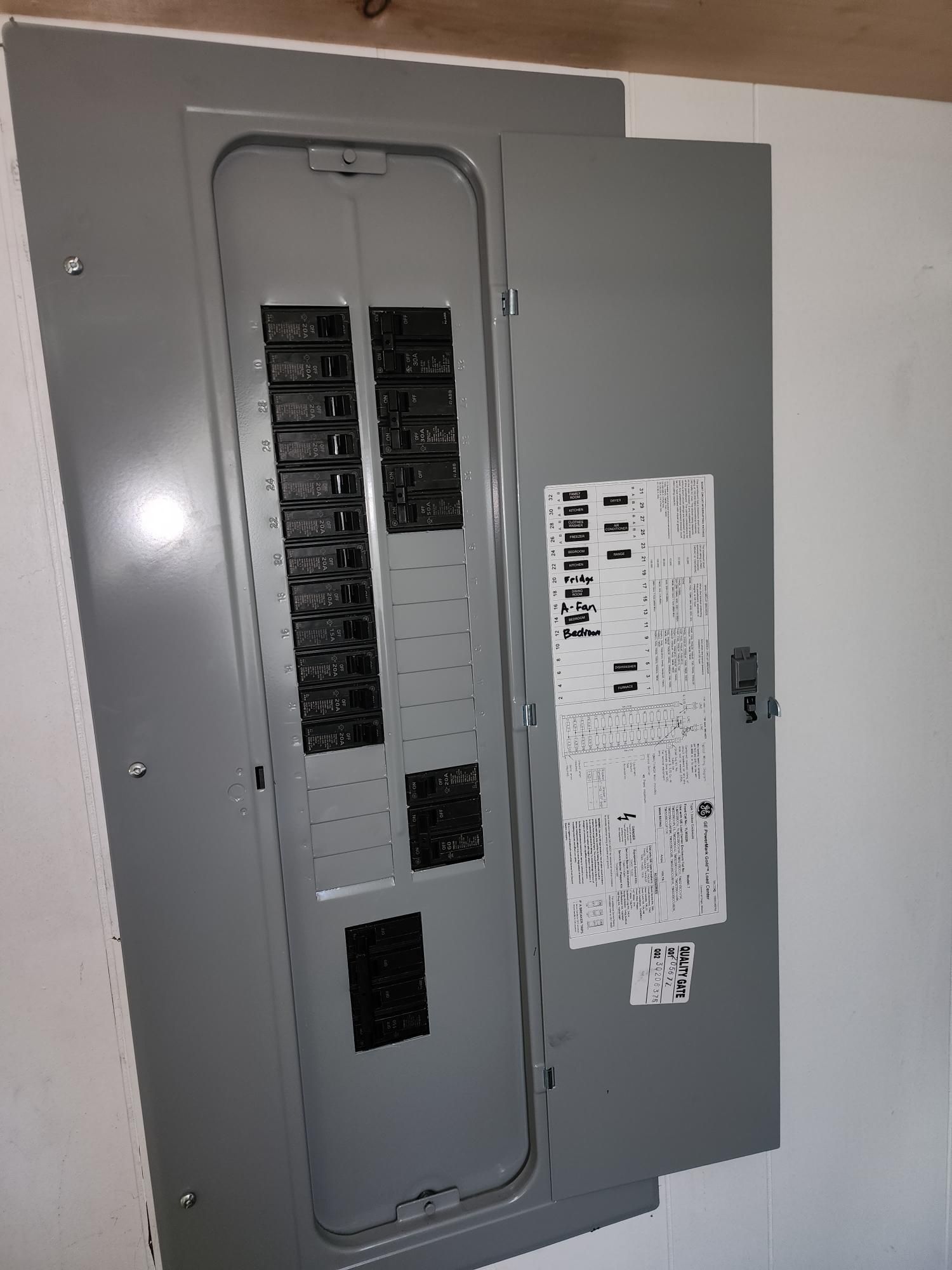 Gray electrical breaker panel with open door and labeled circuits on a wall