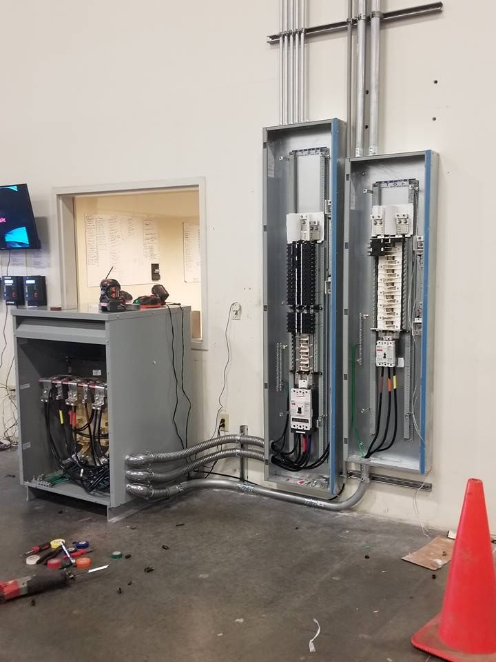 Electrical panels and conduits installed on a white wall in a room, with an open control cabinet.