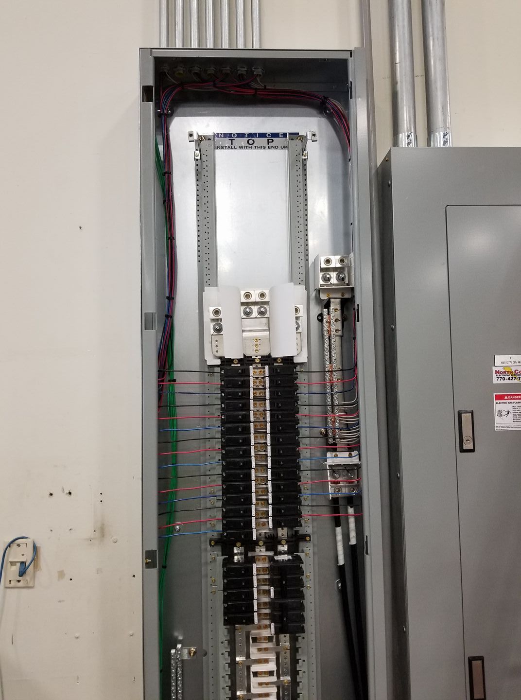 Open electrical panel with numerous wires and breakers. Silver and gray, in a commercial setting.