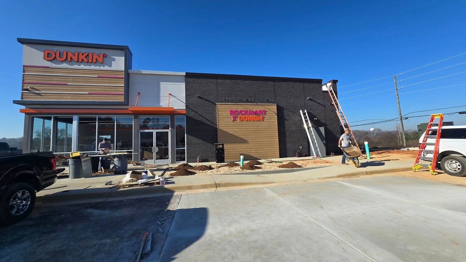 Dunkin' Donuts store under construction; workers on ladders. Building exterior features orange and brown colors.