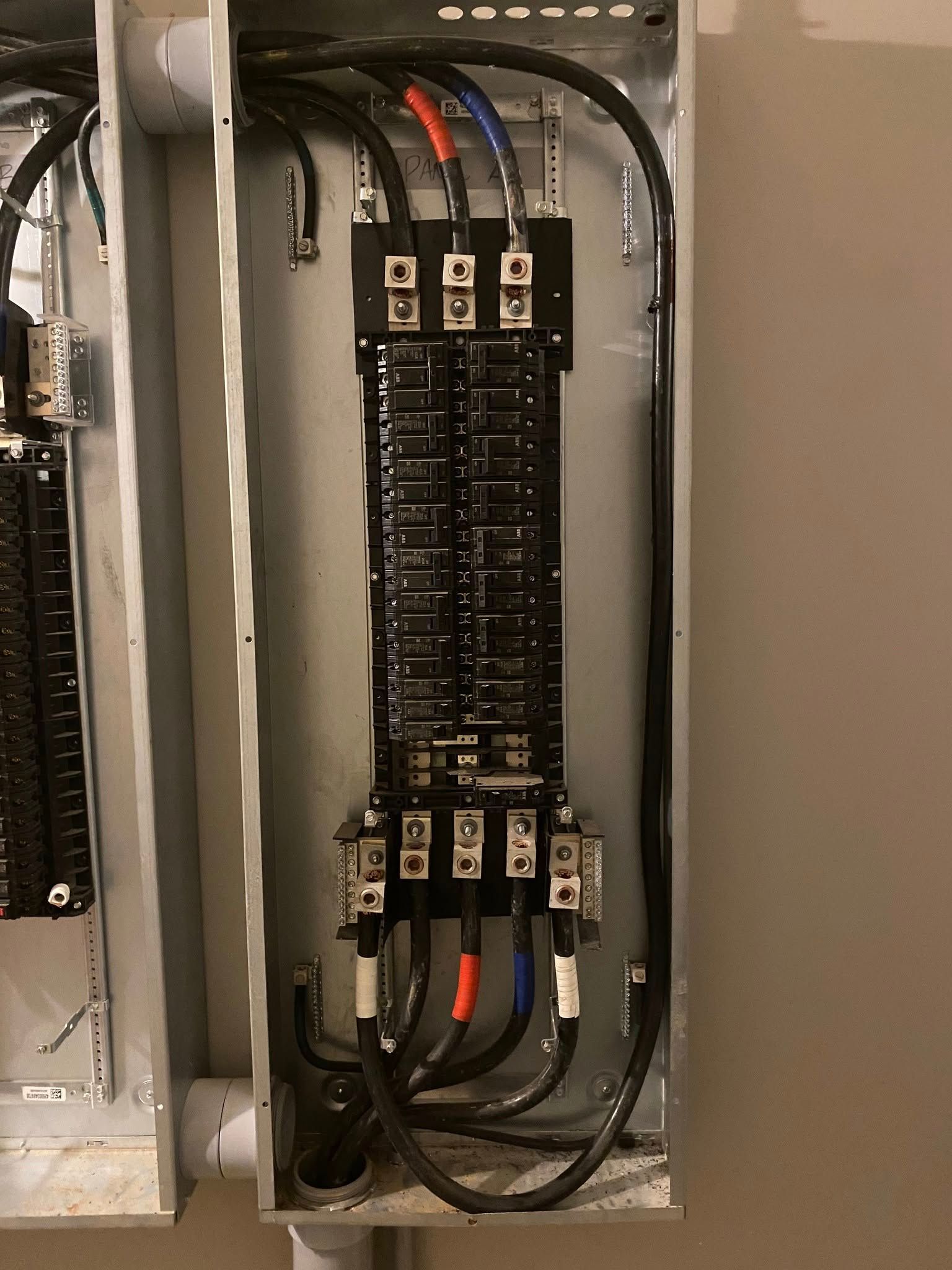 Electrical panel with black wires, circuit breakers, and colored wires, inside a metal box.