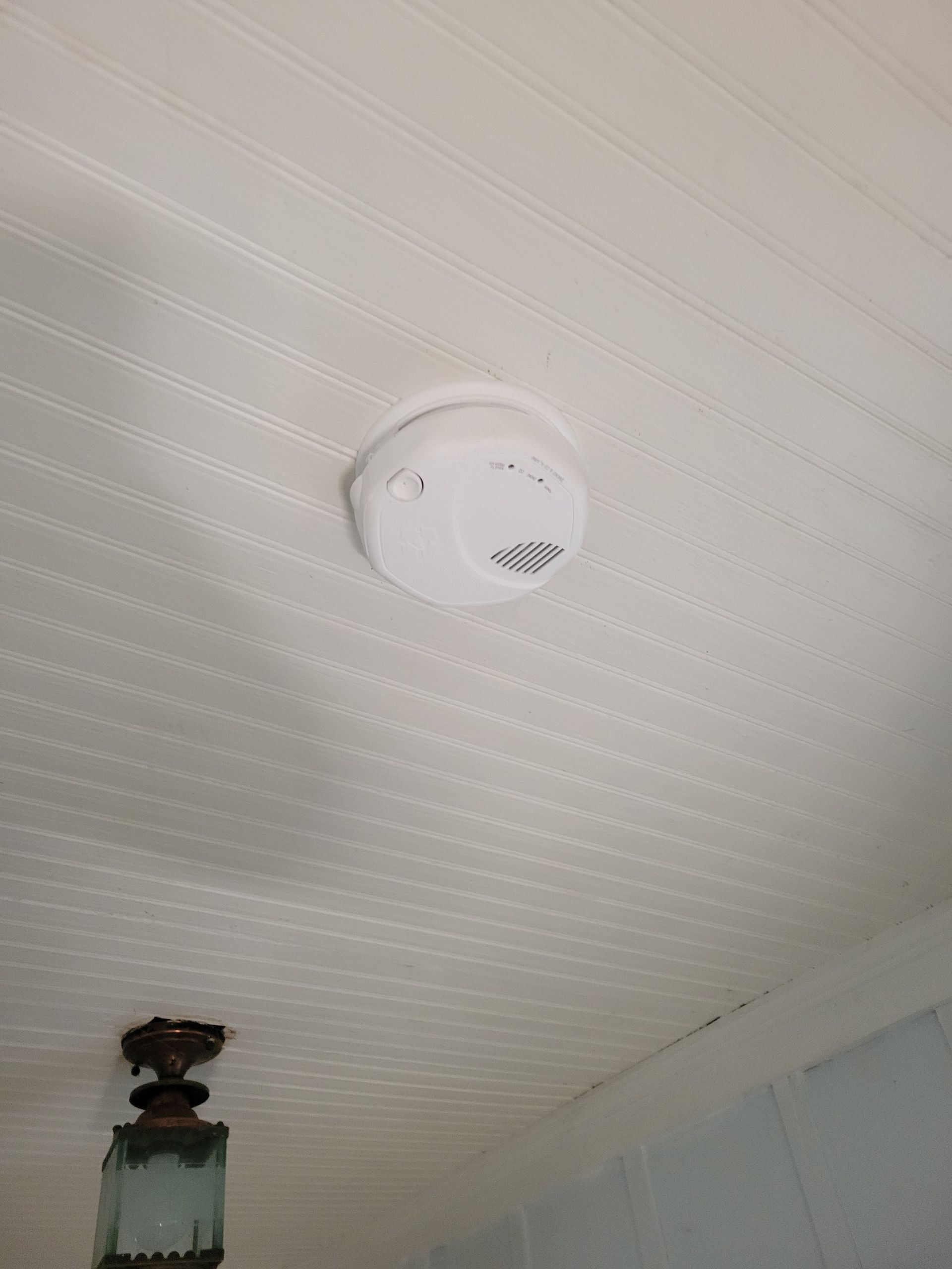 White ceiling with a round smoke detector mounted near the center.