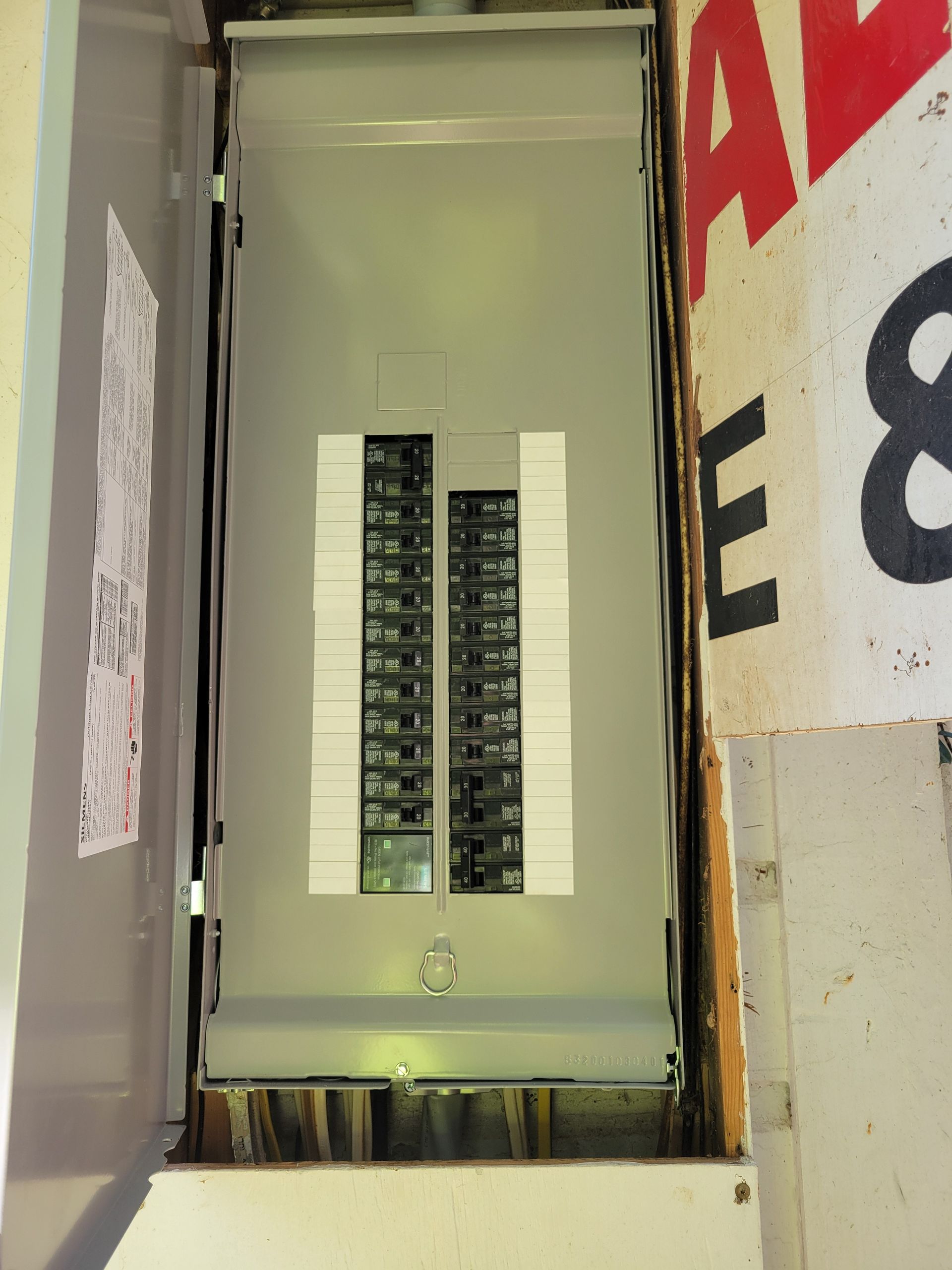 Open electrical panel with exposed circuit breakers in a wall recess.