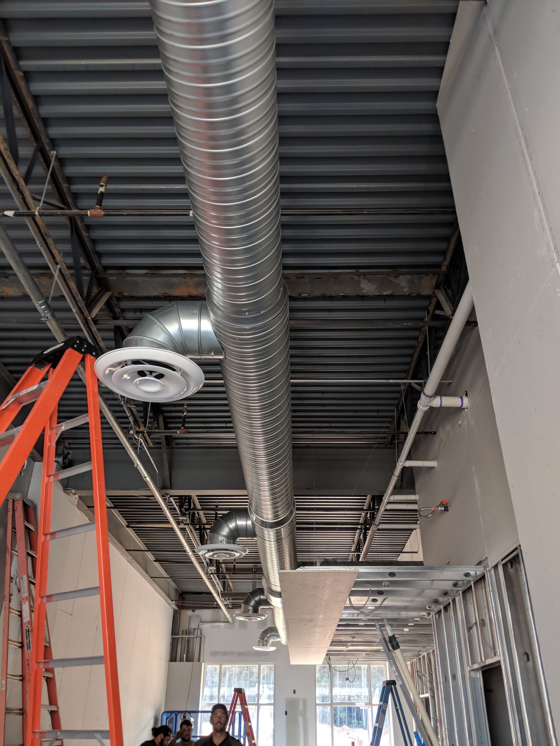Construction site interior with exposed ceiling ductwork and unfinished walls; orange ladder visible.