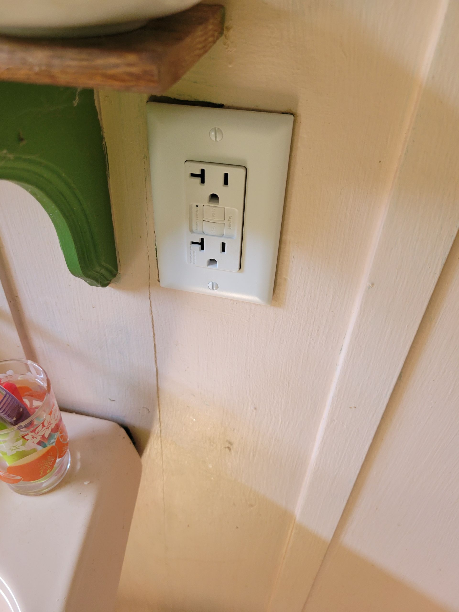 Wall outlet on beige wall beside a green shelf and countertop corner