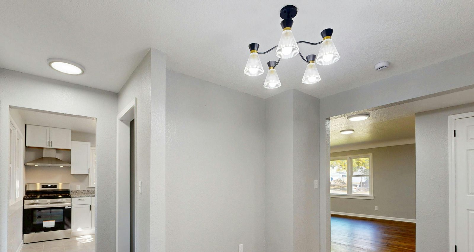 Empty dining area with white walls, ceiling light, and view into kitchen and living room spaces