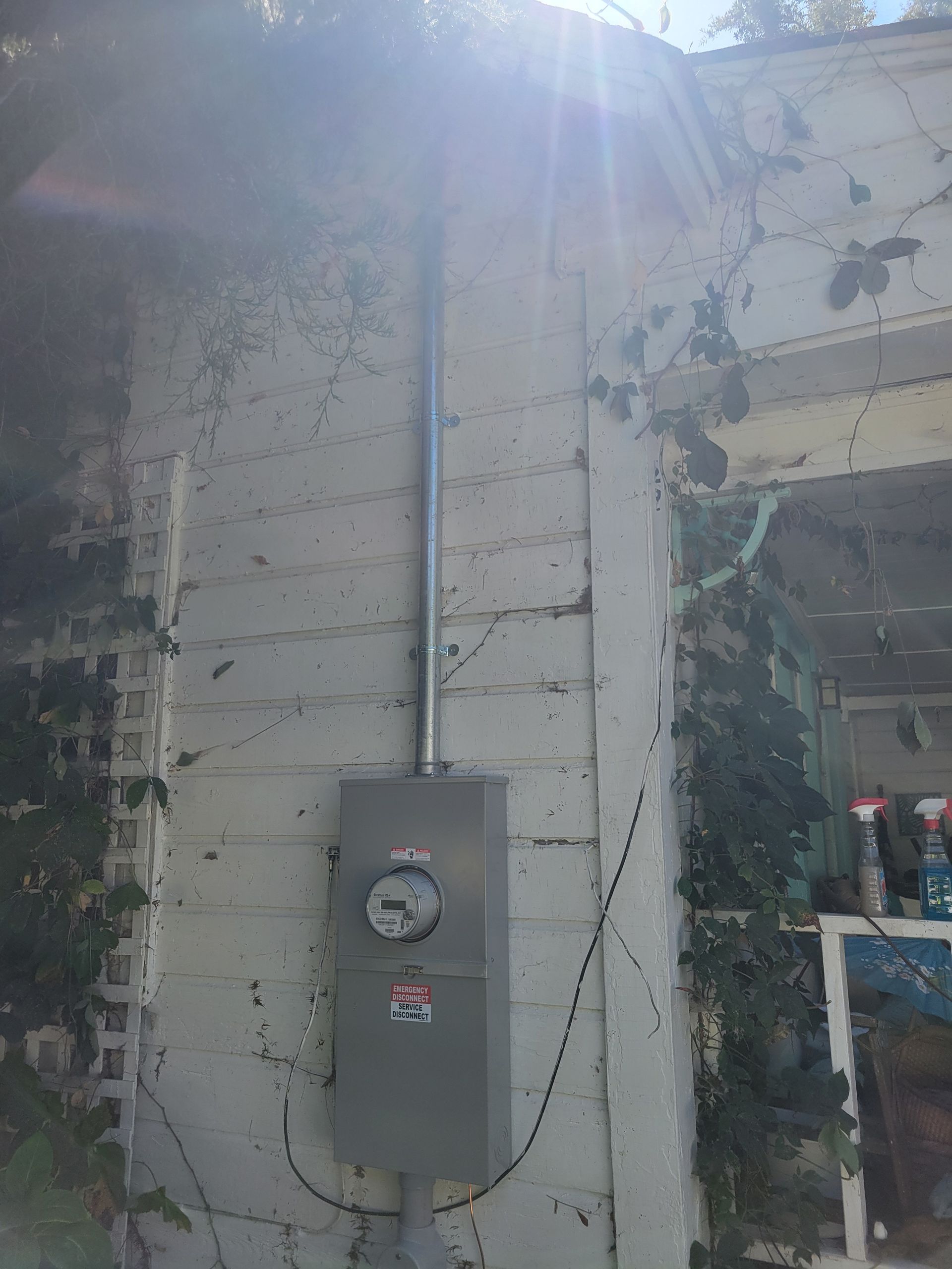 Gray electric meter box on a worn white exterior wall in bright sunlight