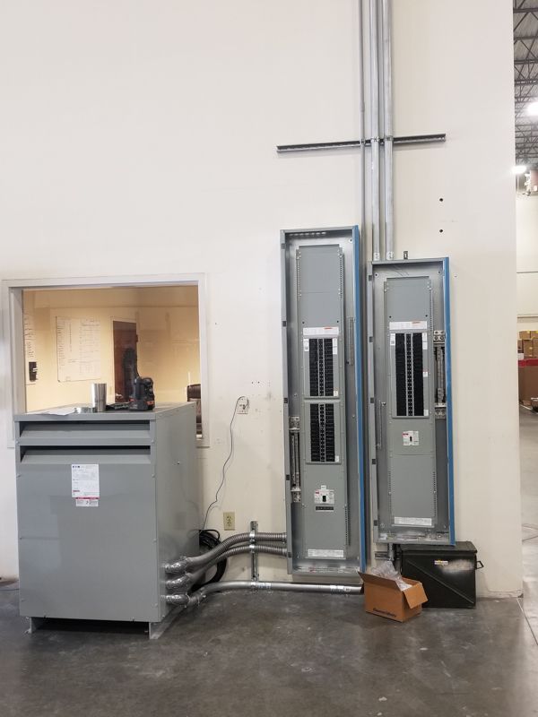 Electrical service room with gray panels, conduit pipes, and a large metal utility box against a white wall