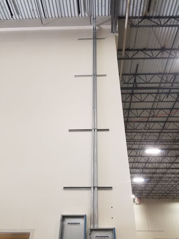 Vertical metal ladder mounted on a white wall in a warehouse with exposed ceiling beams