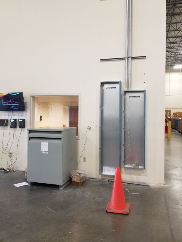 Indoor utility area with a gray cabinet, wall-mounted electrical panels, and an orange traffic cone on the floor