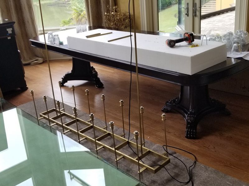 Brass rail kinetic sculpture on a floor in a living room with a white pool table nearby